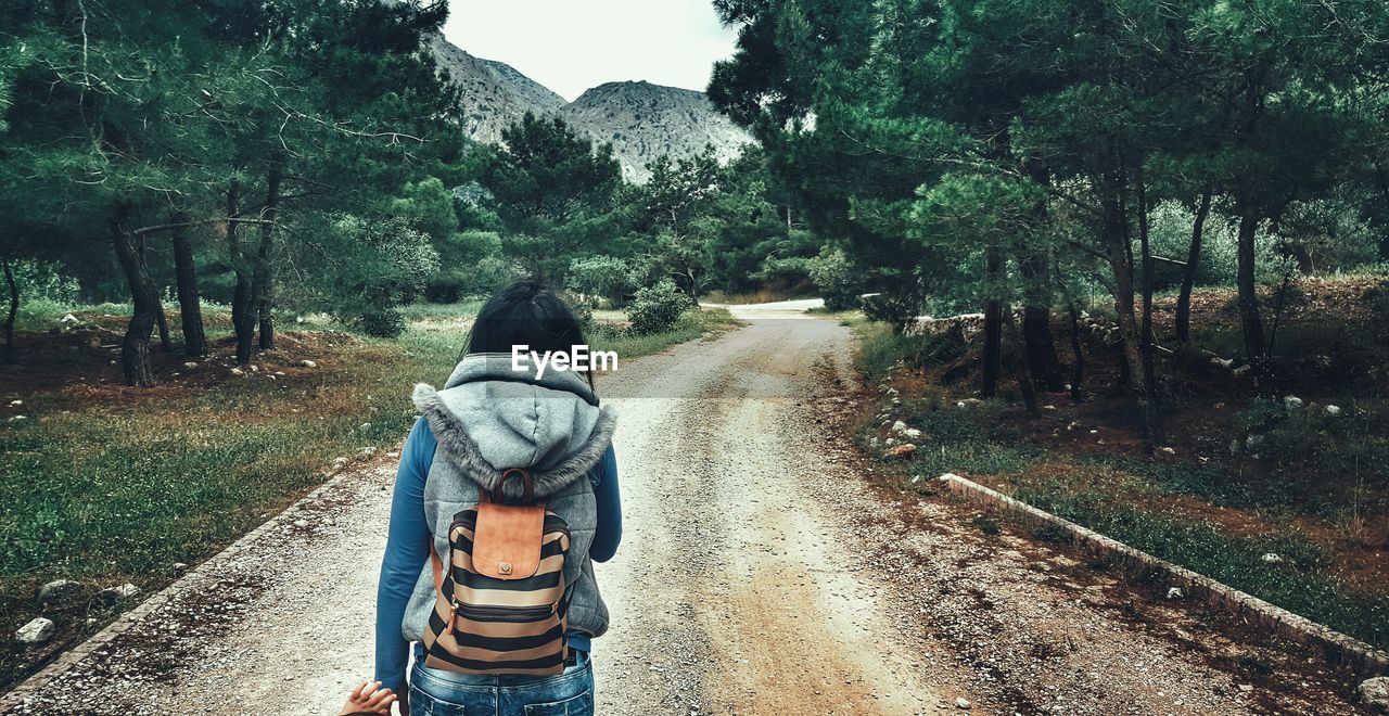 Rear view of female hiker standing on dirt road at field