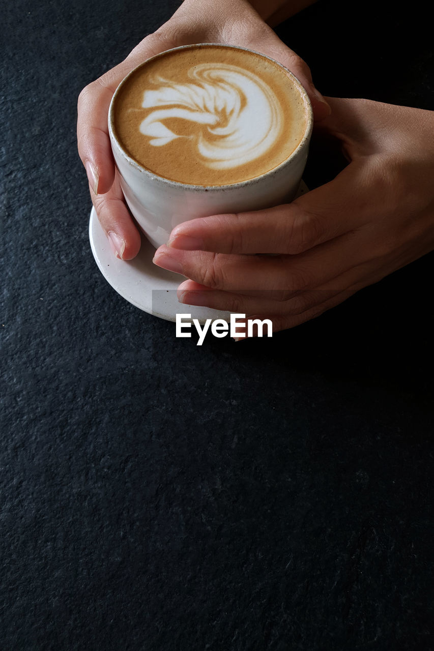 CROPPED IMAGE OF HAND HOLDING COFFEE CUP WITH CAPPUCCINO