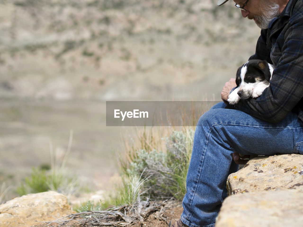 Man holding puppy while sitting on rock