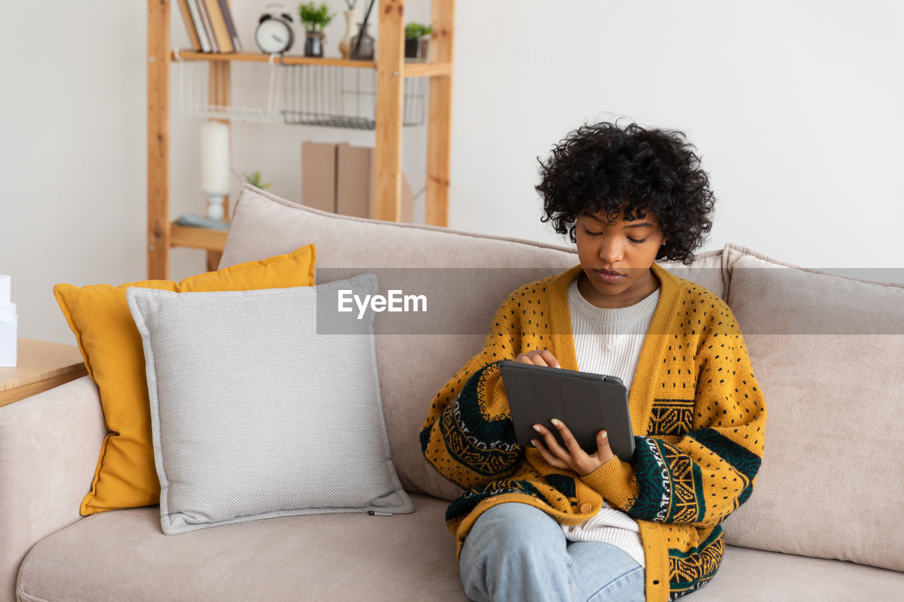 portrait of young woman using digital tablet while lying on bed at home