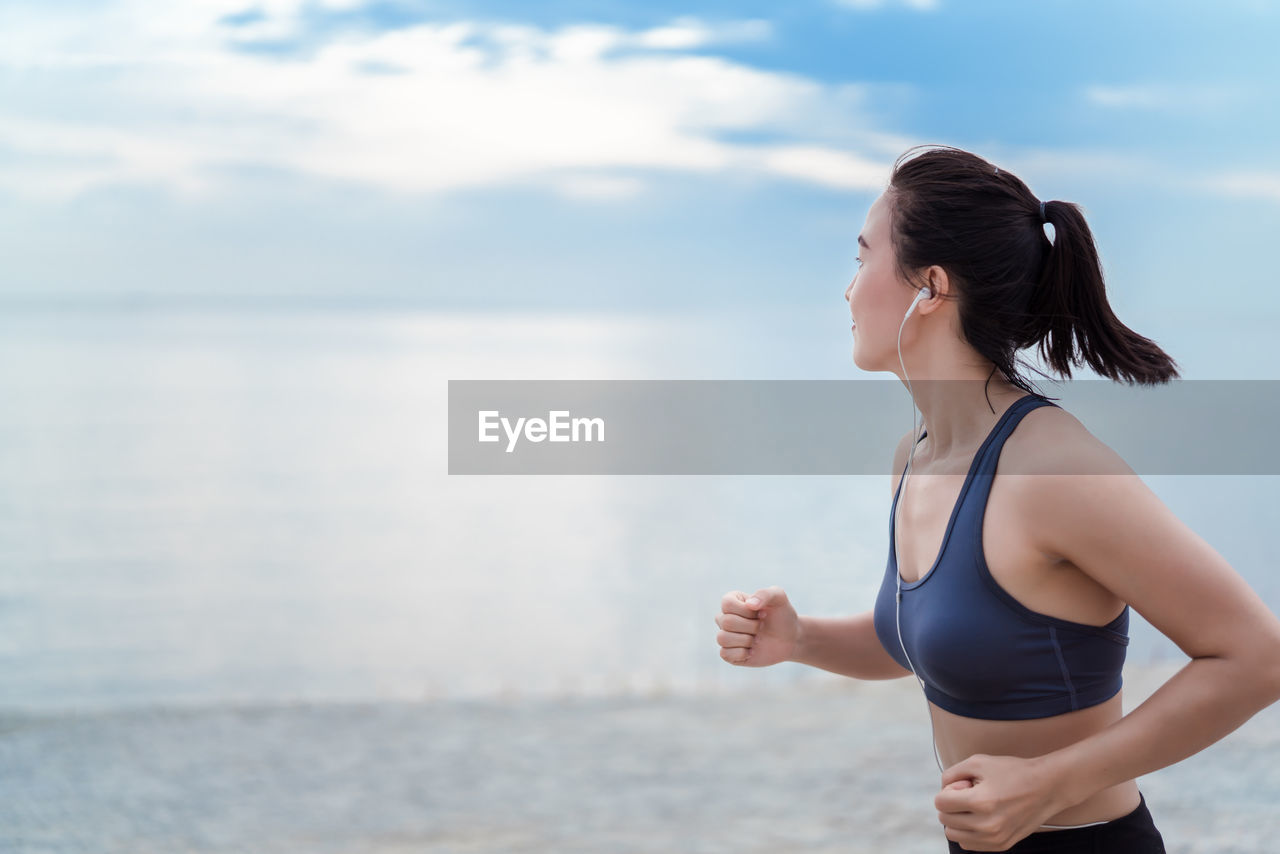 Young woman jogging at beach against sky