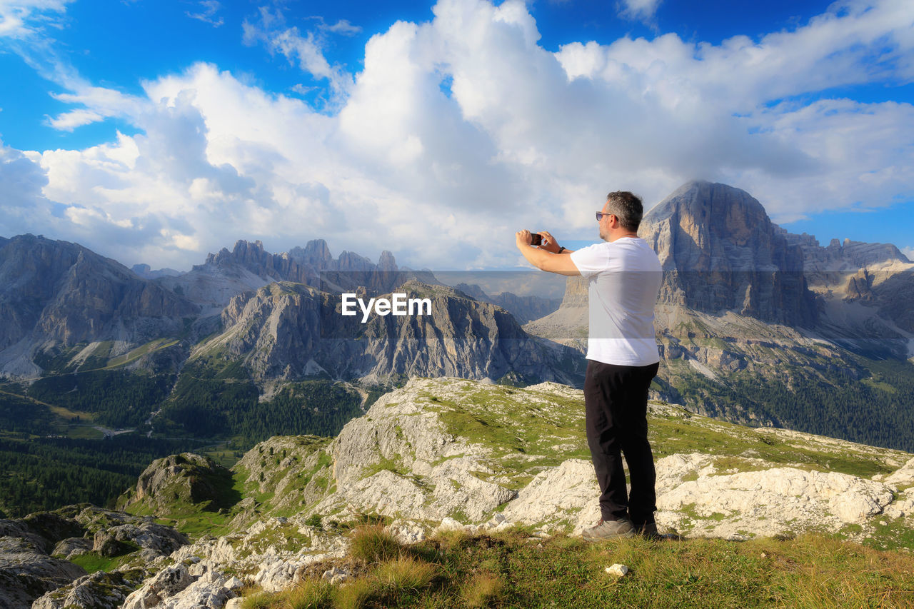 Man standing on cliff against cloudy sky