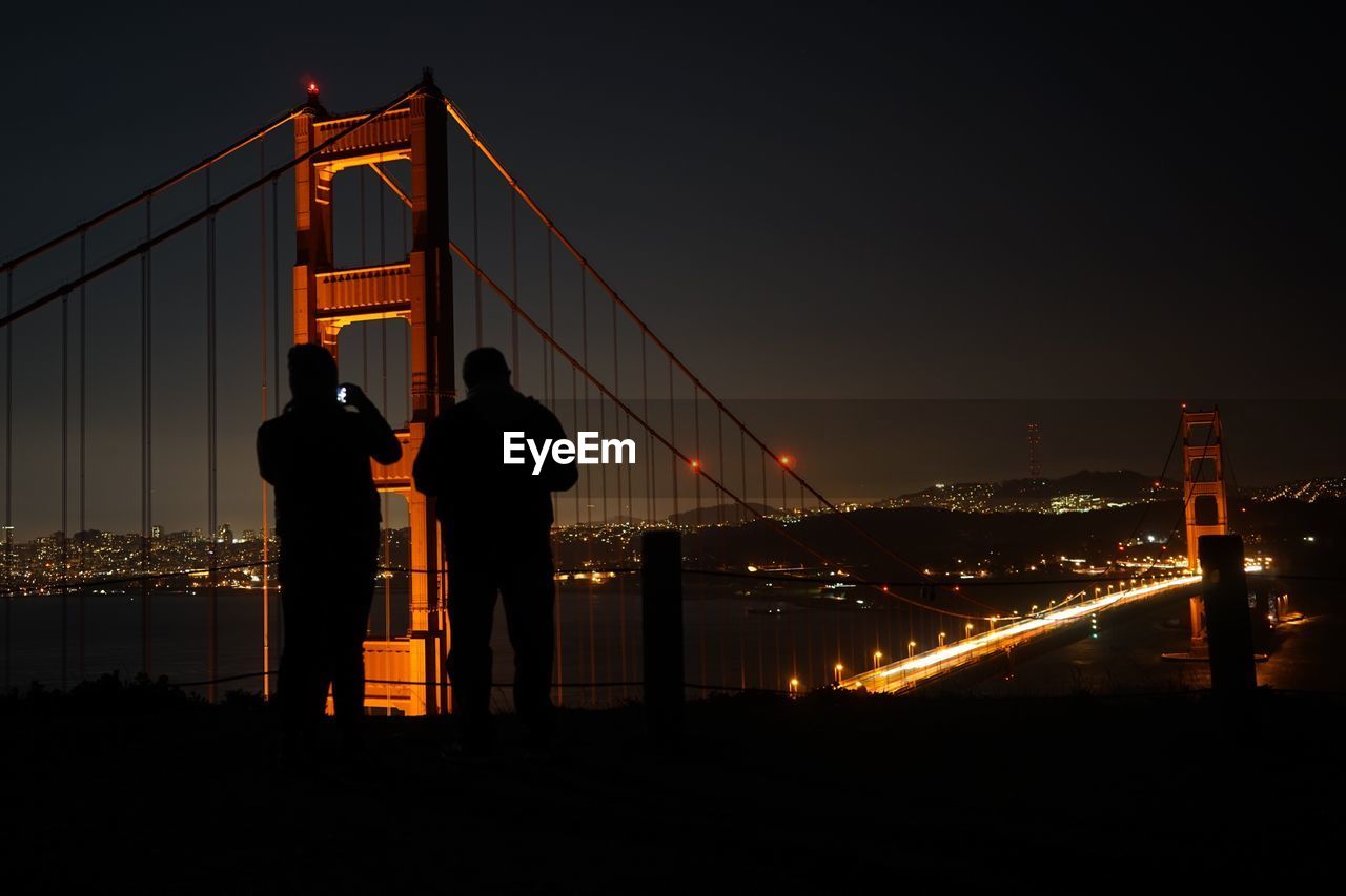 Silhouettes of two men by bridge at night