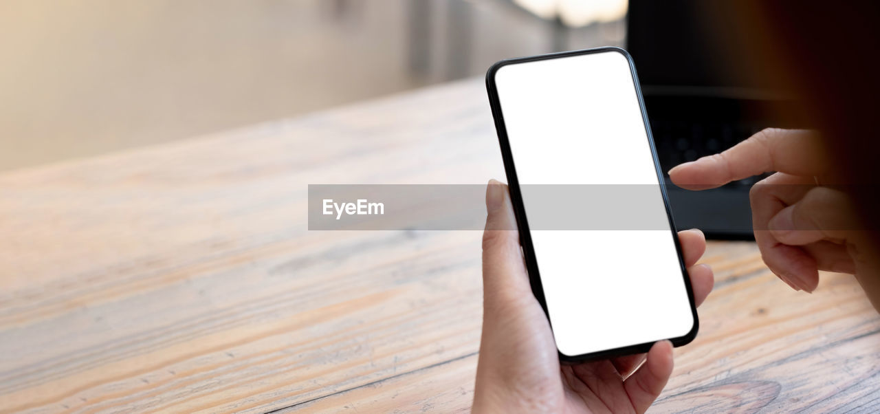 MIDSECTION OF PERSON USING SMART PHONE ON TABLE