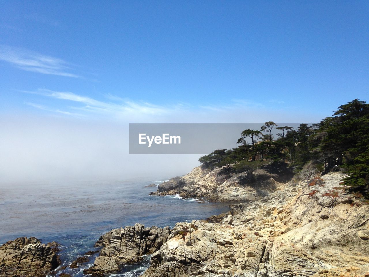 ROCKS BY SEA AGAINST BLUE SKY