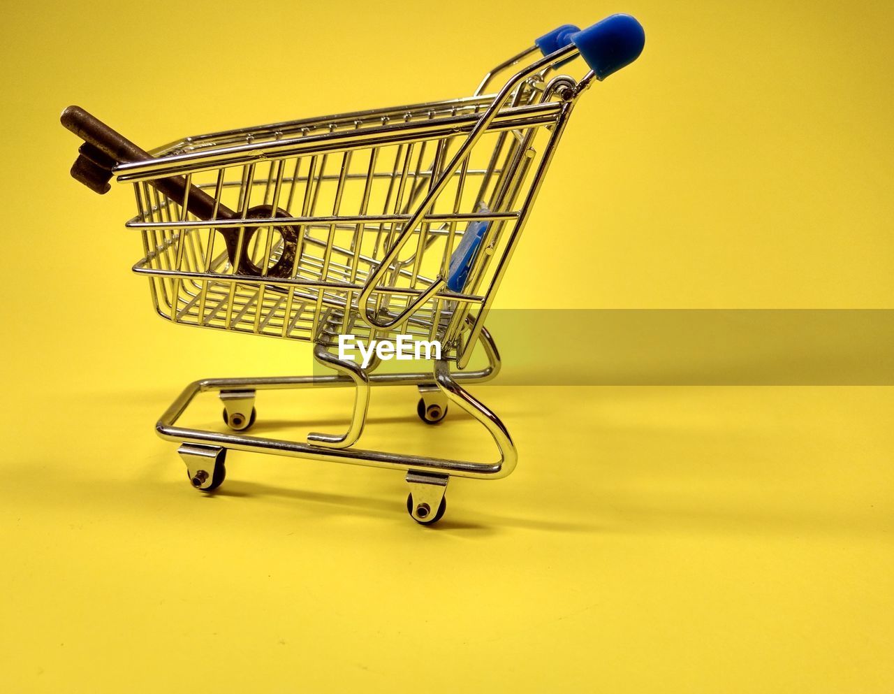 Close-up of shopping cart and key on yellow background
