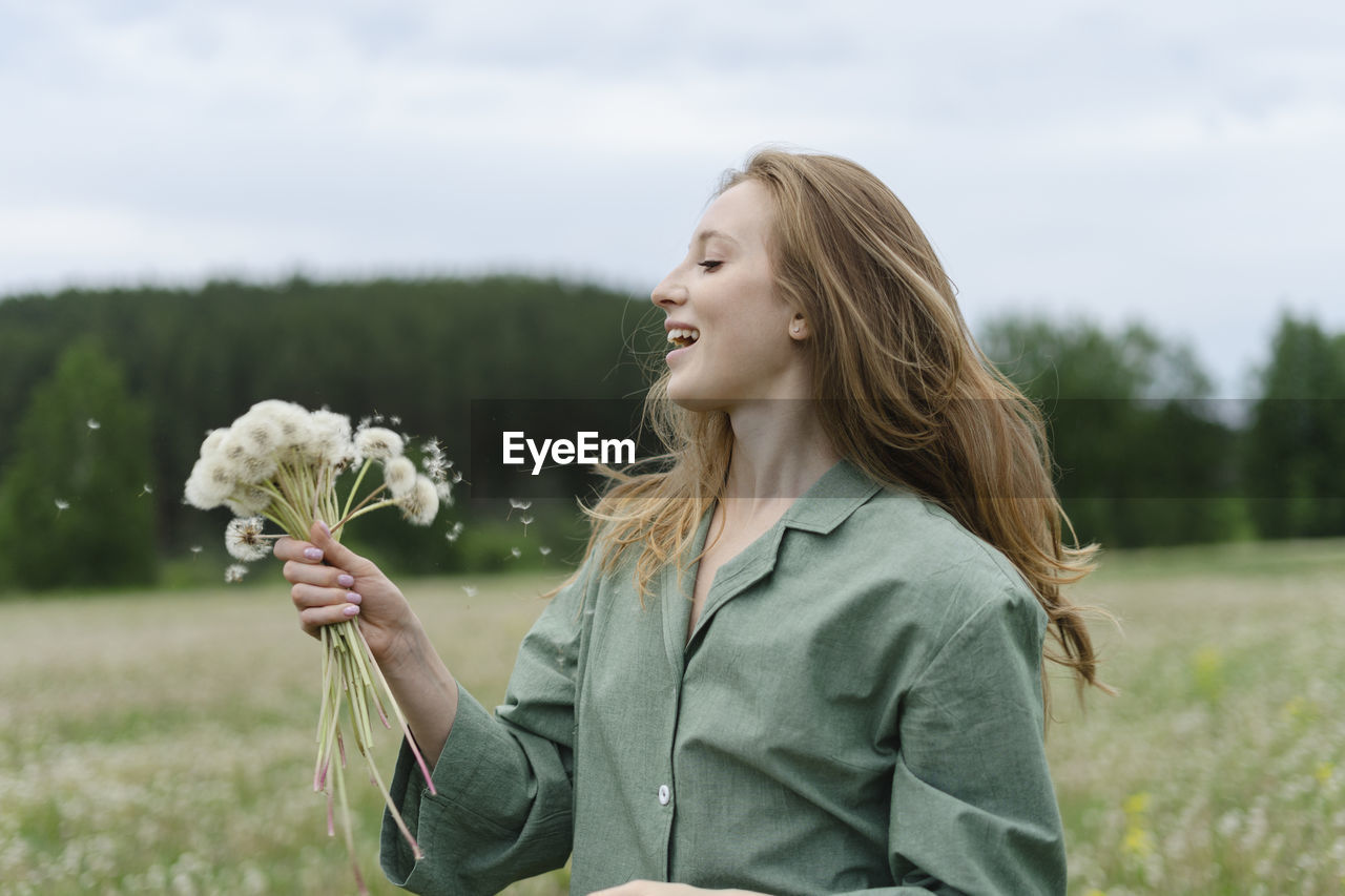 Smiling young woman holding dandelions on field