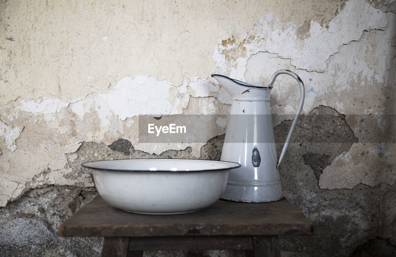 Close-up of old wash basin and water jar against wall at home