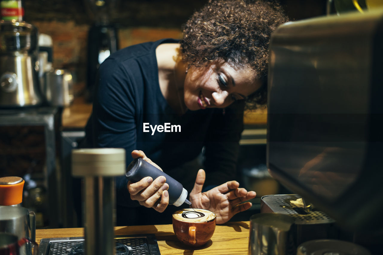 Male waitress barista working in coffee shop. prepare decorated coffee