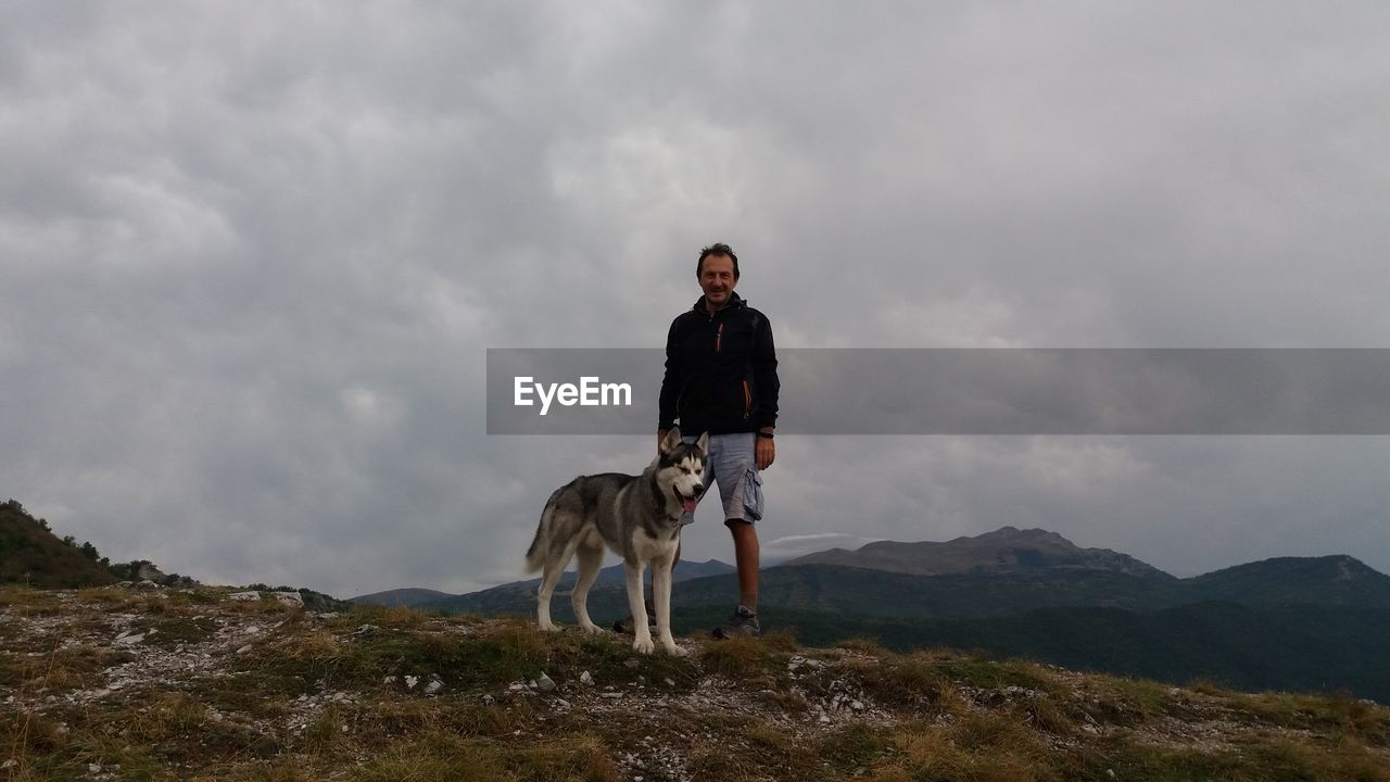 Portrait of man with dog standing on mountain against sky