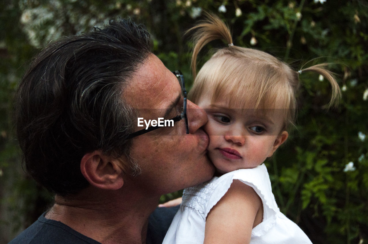 Close-up of father kissing daughter against tree