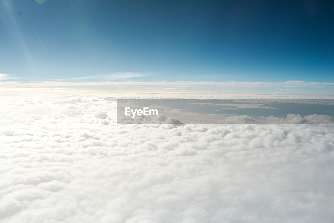 sky, cloud, cloudscape, aerial view, blue, nature, flying, horizon, environment, atmosphere, beauty in nature, scenics - nature, airplane, white, fluffy, high up, no people, air vehicle, above, copy space, idyllic, outdoors, sunlight, travel, day, dramatic sky, tranquility, backgrounds, tranquil scene, overcast, transportation, high angle view, landscape, space, mid-air, awe, softness, ethereal, dreamlike, urban skyline, wind, window, snow