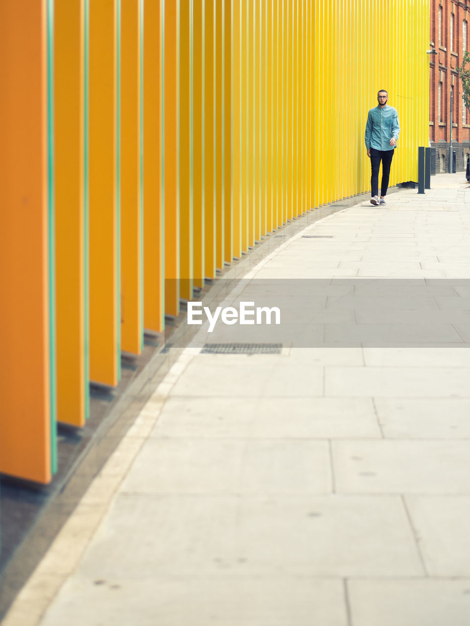 Man walking on footpath by modern yellow building in city