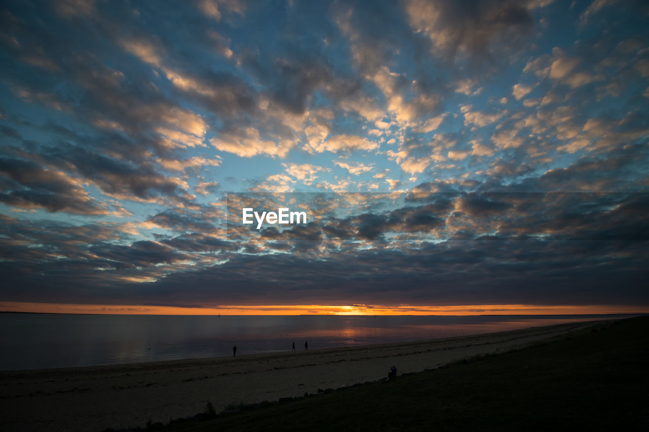 SCENIC VIEW OF BEACH AGAINST DRAMATIC SKY DURING SUNSET