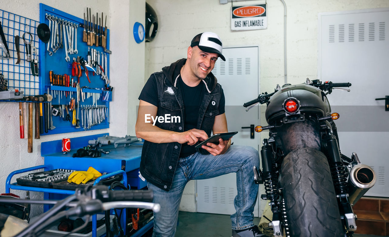 Portrait of man leaning by motorcycle in garage