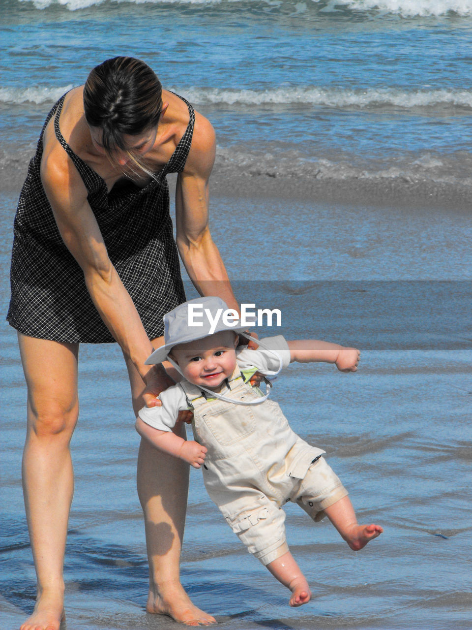 Mother carrying cute baby boy while standing at beach