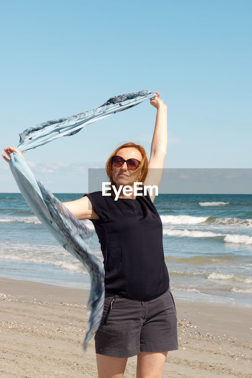 Woman wearing sunglasses while standing at beach against sky