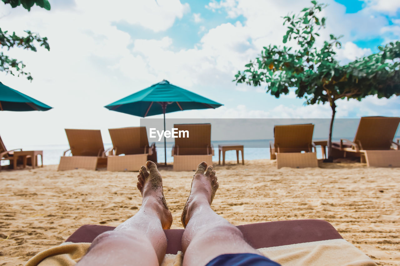 Low section of man relaxing at beach against sky