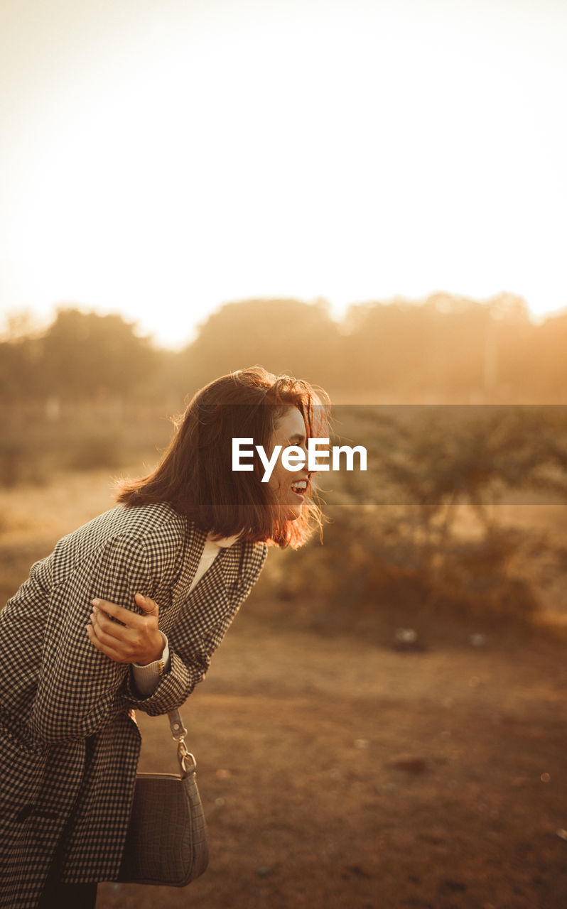 Young woman looking away against sky during sunset