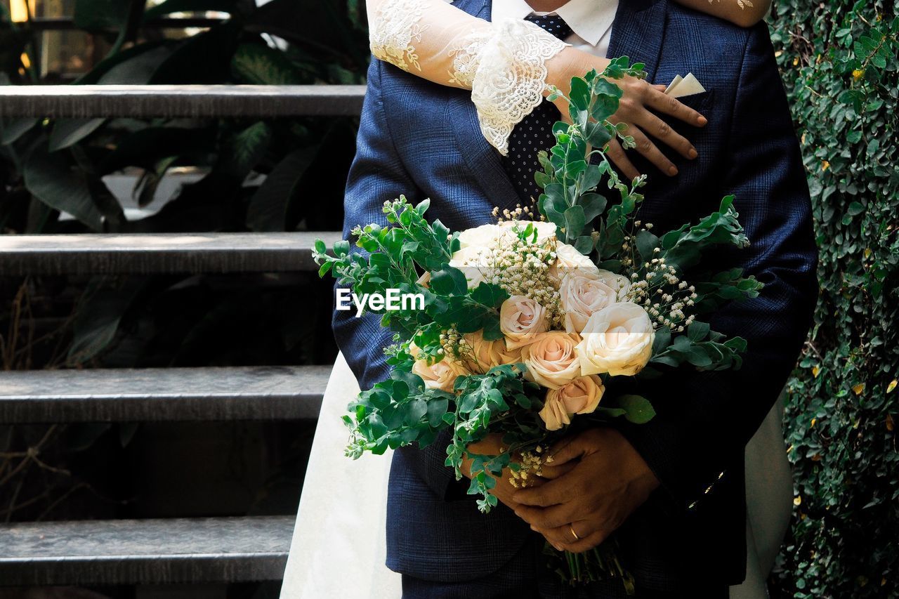 Cropped hands of bride with bridegroom holding bouquet during wedding ceremony