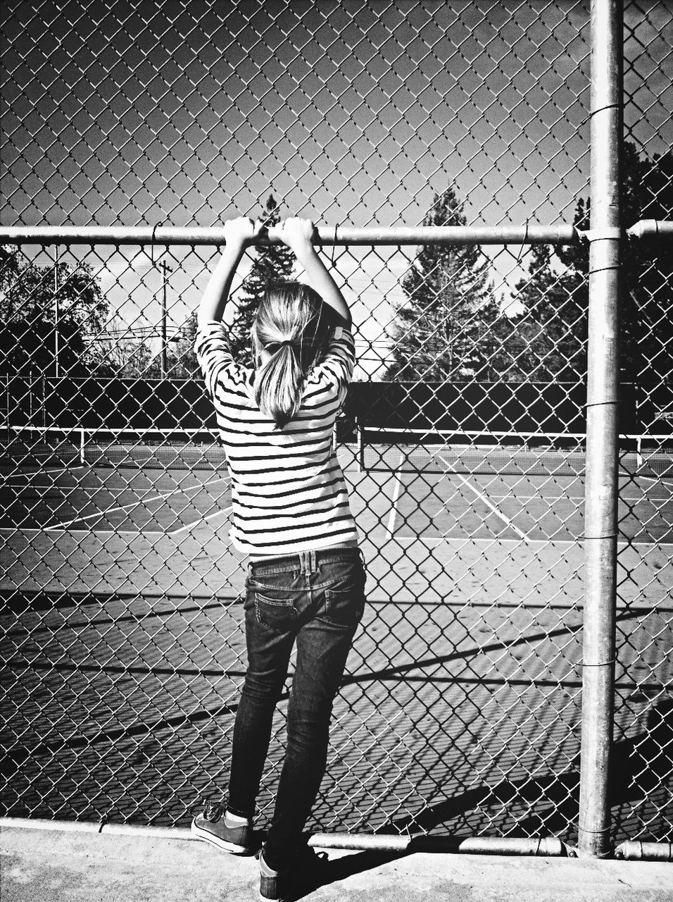 Full length rear view of girl standing in front of chainlink fence