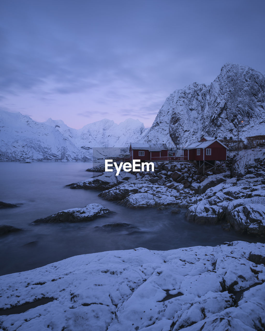 Red rorbu cabins on snow covered rocky coastline, hamnøy, lofoten islands, norway