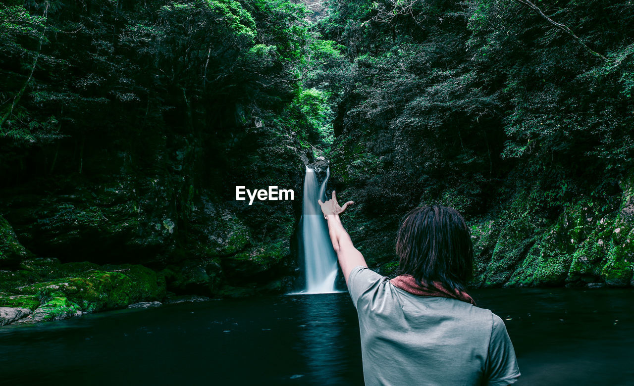 Rear view of man doing hand sign against waterfall