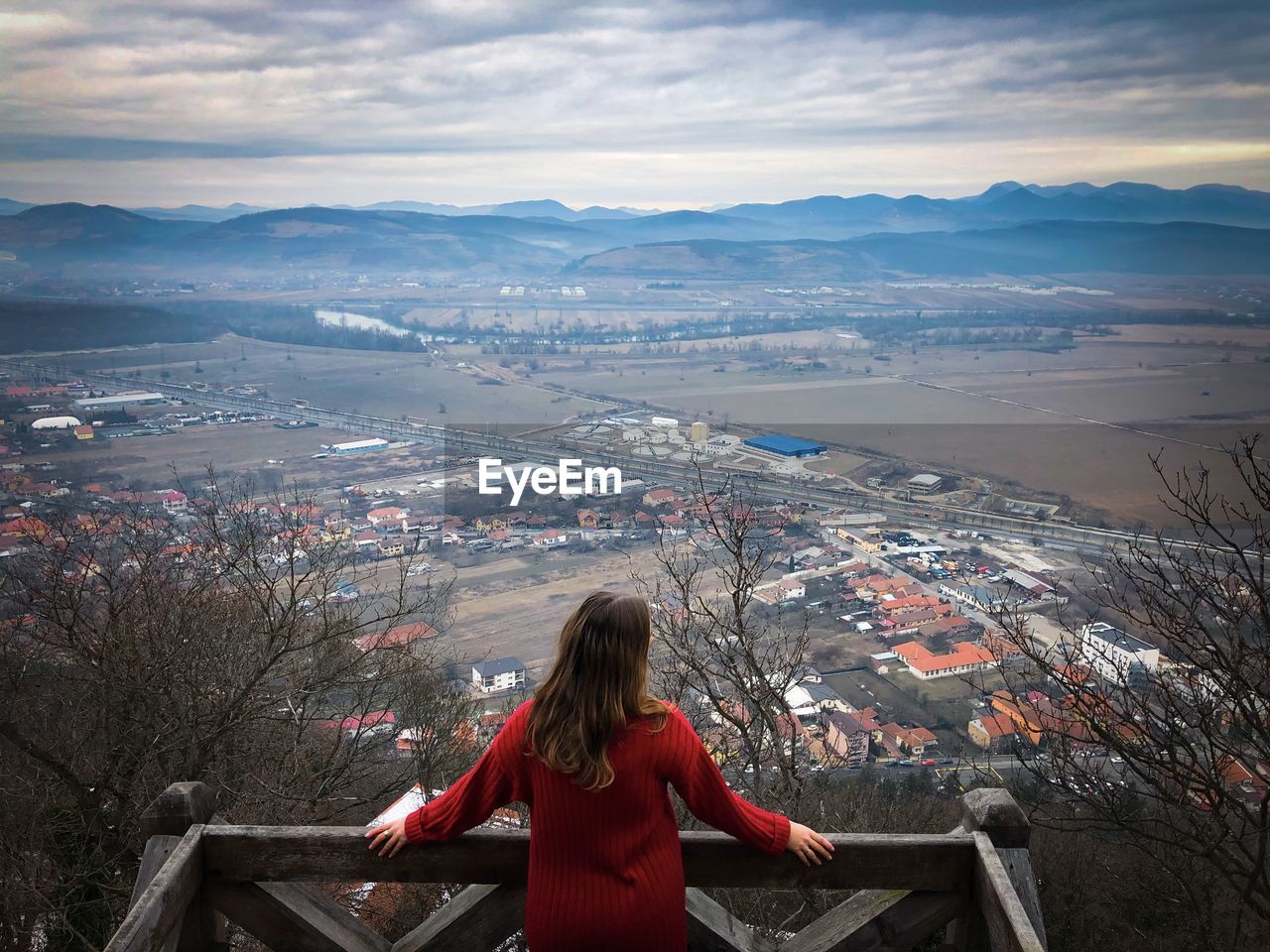 Rear view of young woman in red sweater looking down at the city from the top of a hill