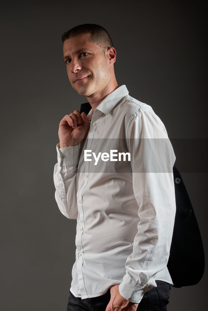 one person, studio shot, adult, formal wear, men, tuxedo, portrait, white, indoors, clothing, standing, young adult, dress shirt, shirt, outerwear, button down shirt, spring, waist up, sleeve, three quarter length, person, looking at camera, collar, business, black background, emotion, looking, cut out, photo shoot, businessman, gray, fashion