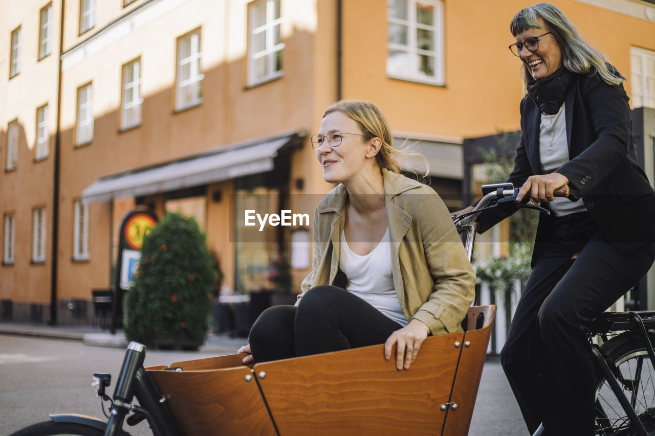 Happy mature businesswoman riding cargo bicycle with female colleague in city