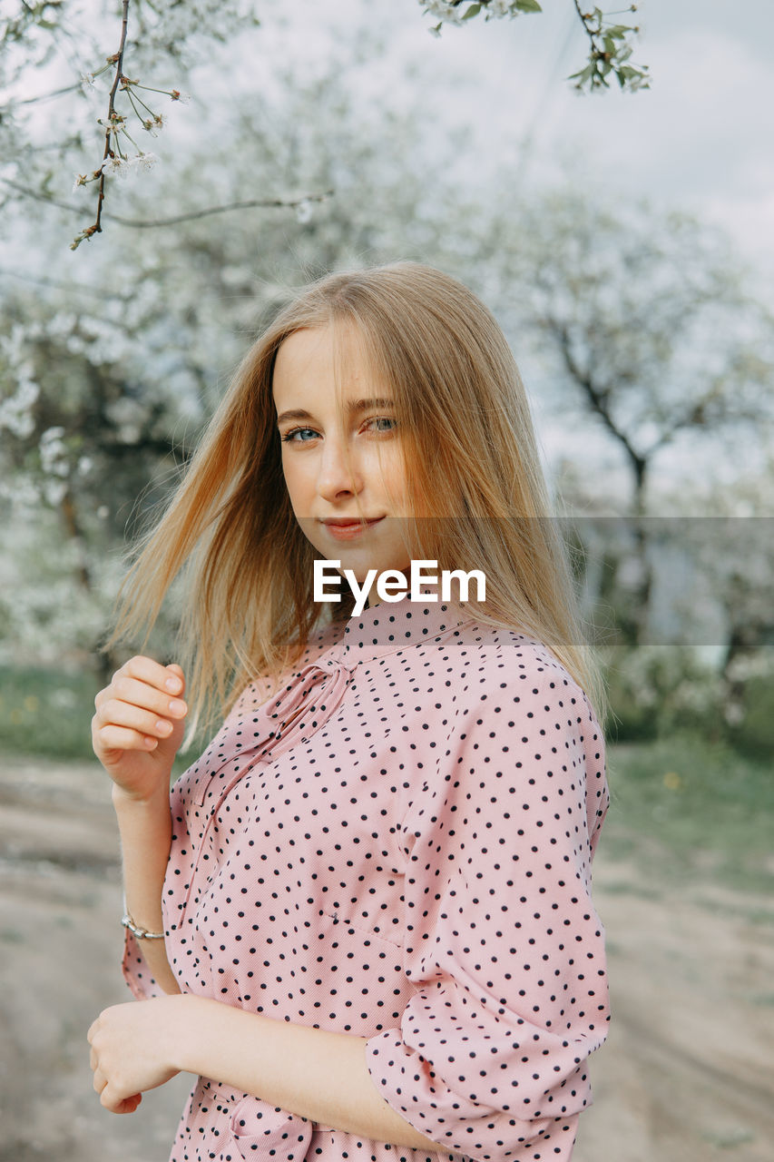 Blonde girl on a spring walk in the garden with cherry blossoms. female portrait, close-up. 