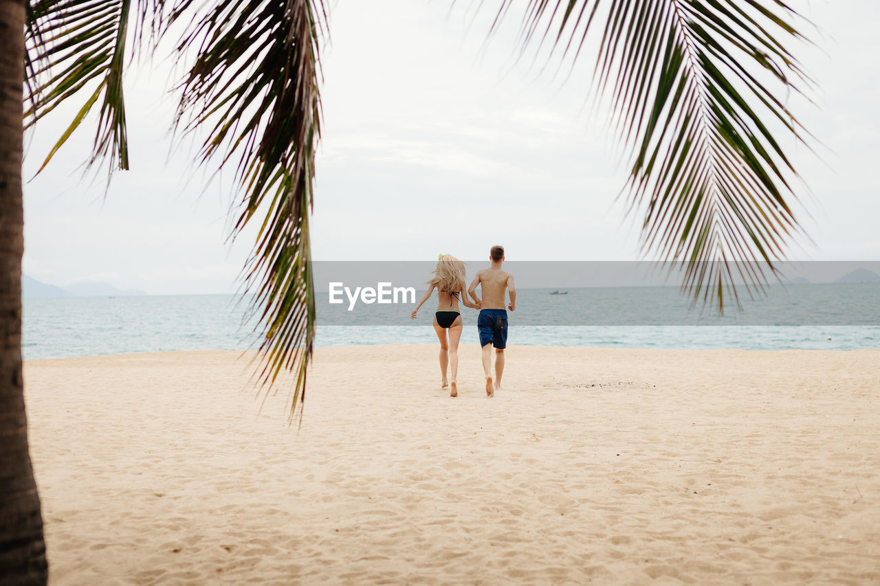 Rear view of couple running on beach against sky