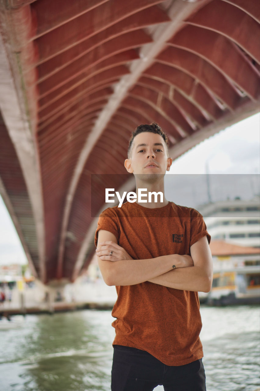 FULL LENGTH OF A YOUNG MAN STANDING AGAINST BUILT STRUCTURE