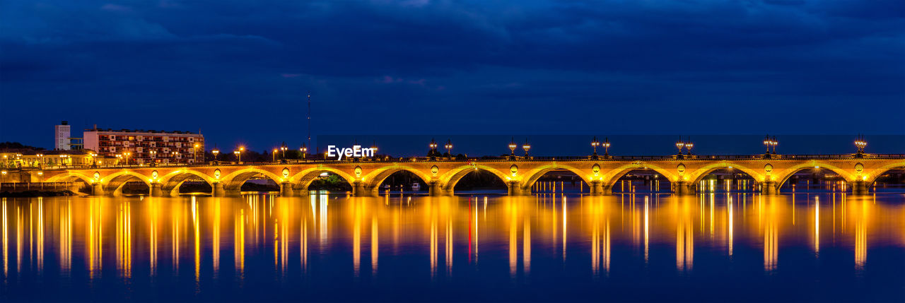 ILLUMINATED BRIDGE OVER RIVER AGAINST BLUE SKY