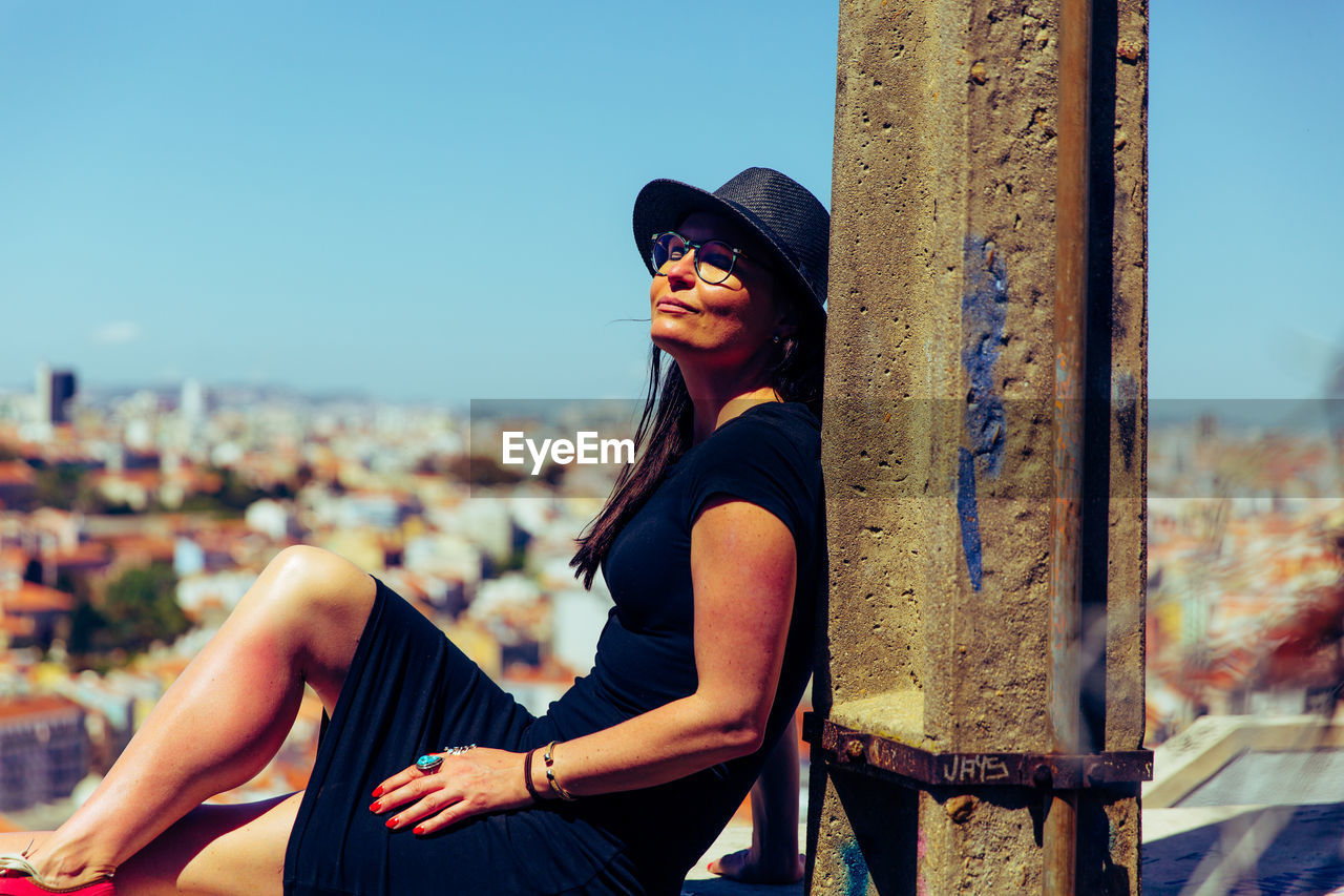 PORTRAIT OF YOUNG WOMAN SITTING AGAINST CITYSCAPE