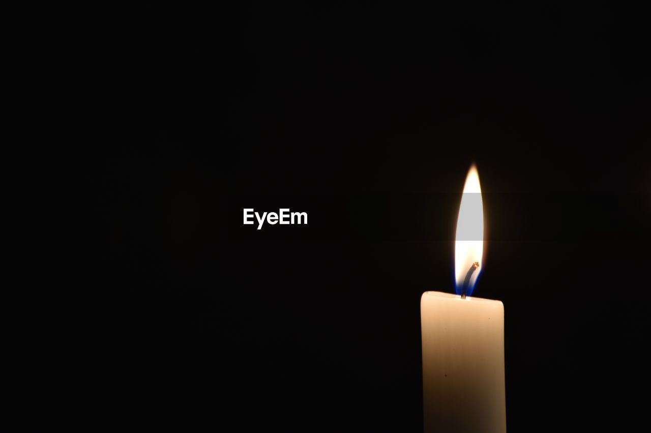 Close-up of burning candle against black background