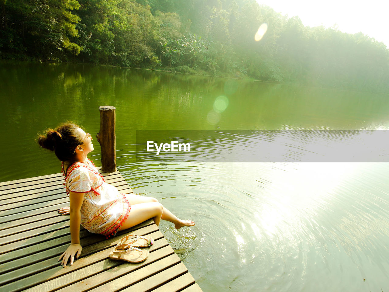 Woman sitting on pier over lake in sunny day