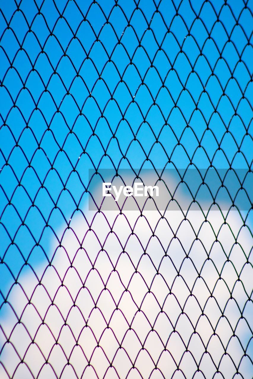 Low angle view of chainlink fence against blue sky