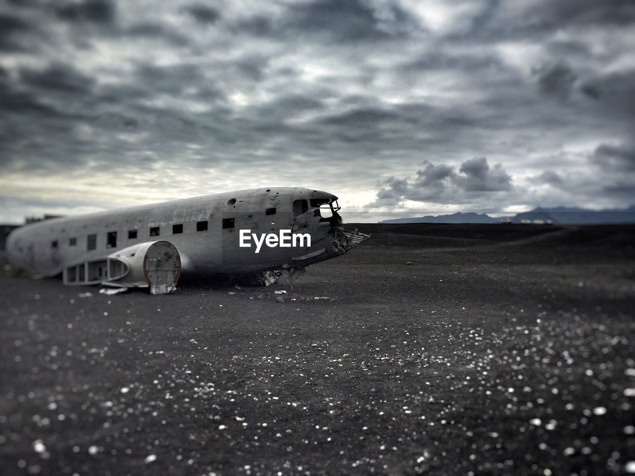 Damaged airplane on field against cloudy sky