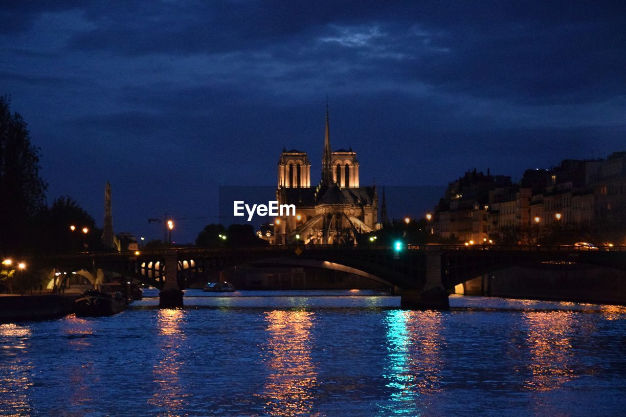 Illuminated bridge over river against sky in city at night