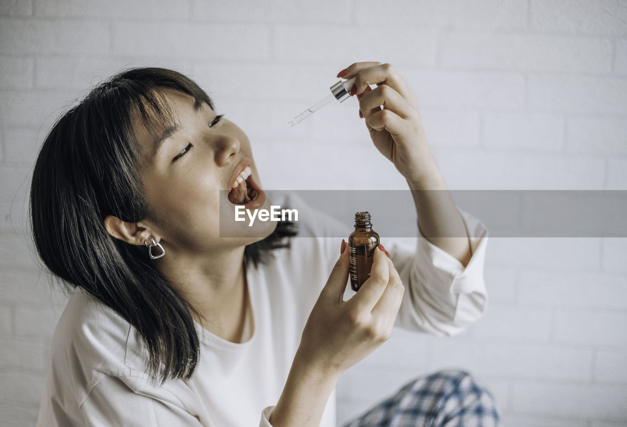 Asian woman dripping cbd oil into mouth for sleep. medical cannabis. vitamins and supplements