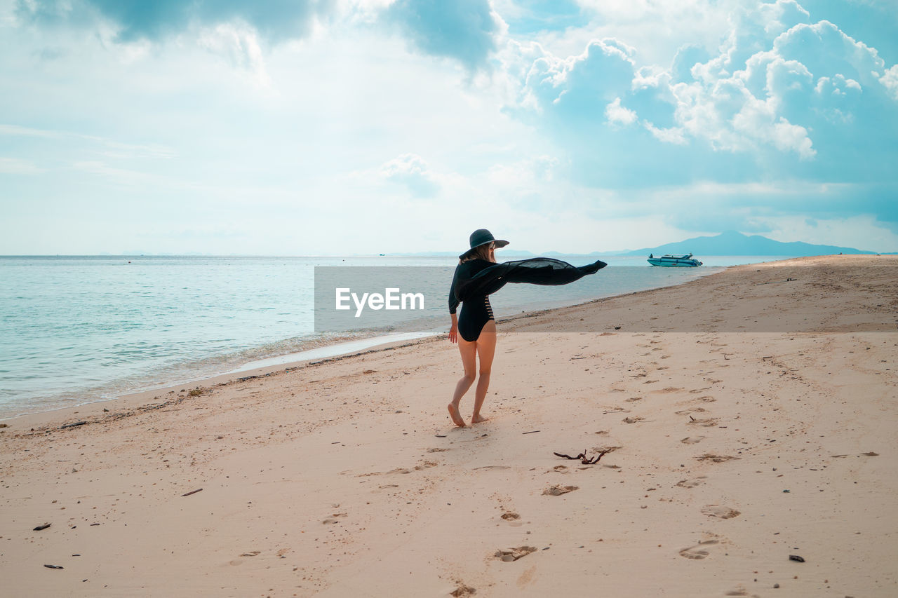 Full length of woman walking on shore at beach against sky