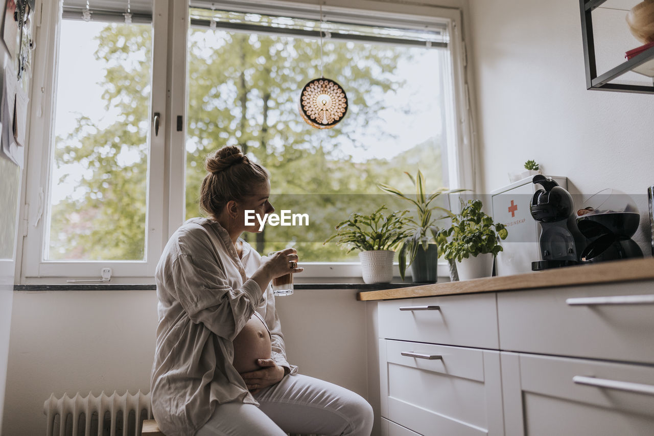 Pregnant woman drinking coffee in kitchen