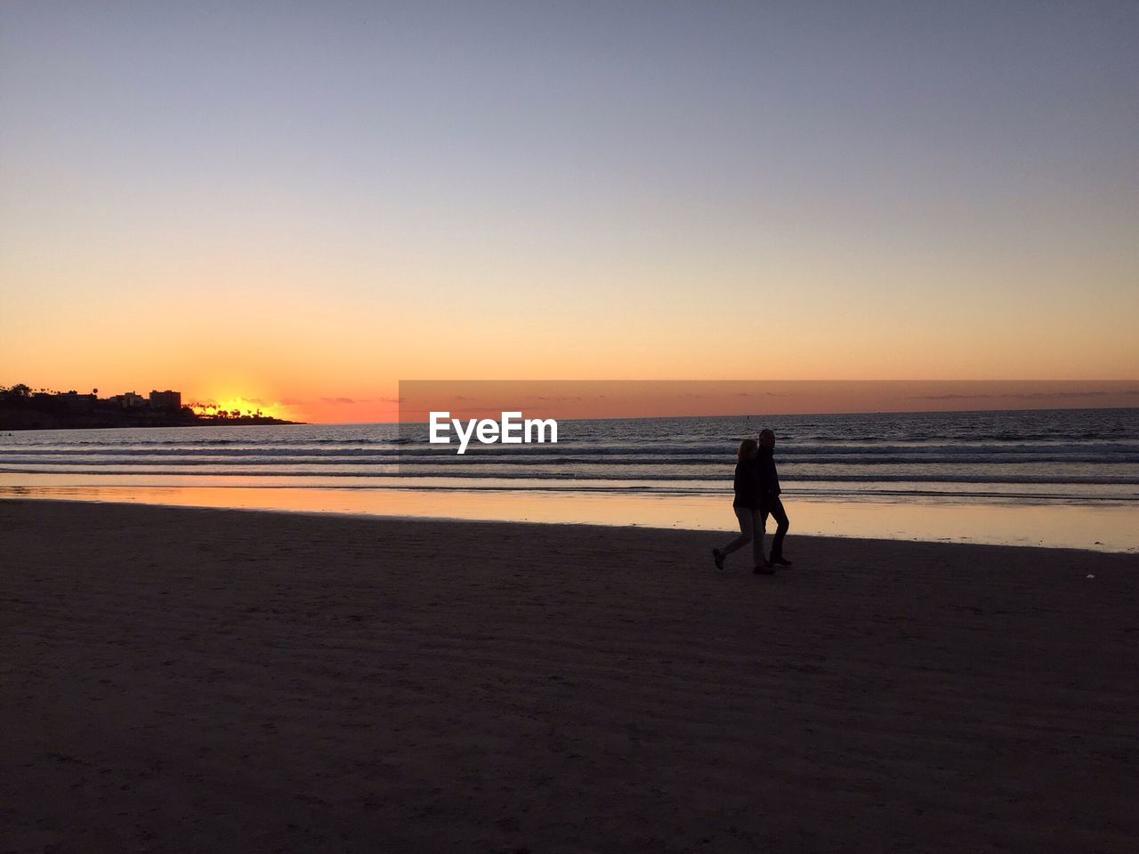 People walking on beach against clear sky at sunset