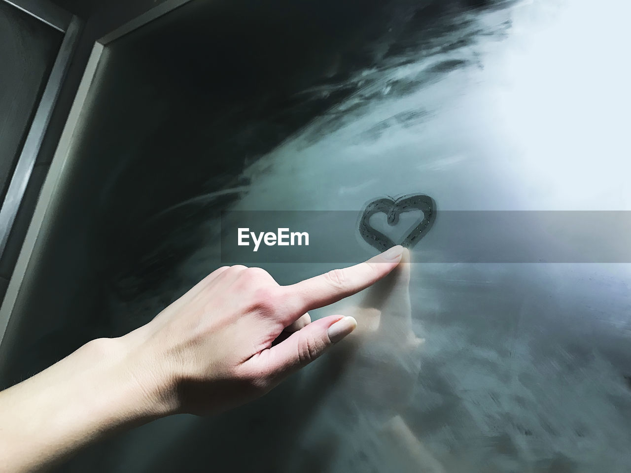 Cropped hand of woman drawing heart shape on wet mirror