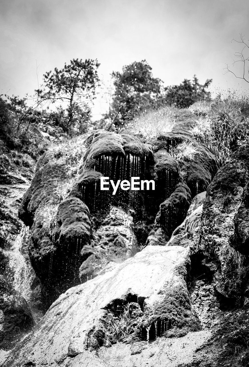 Low angle view of water flowing from rocks against sky