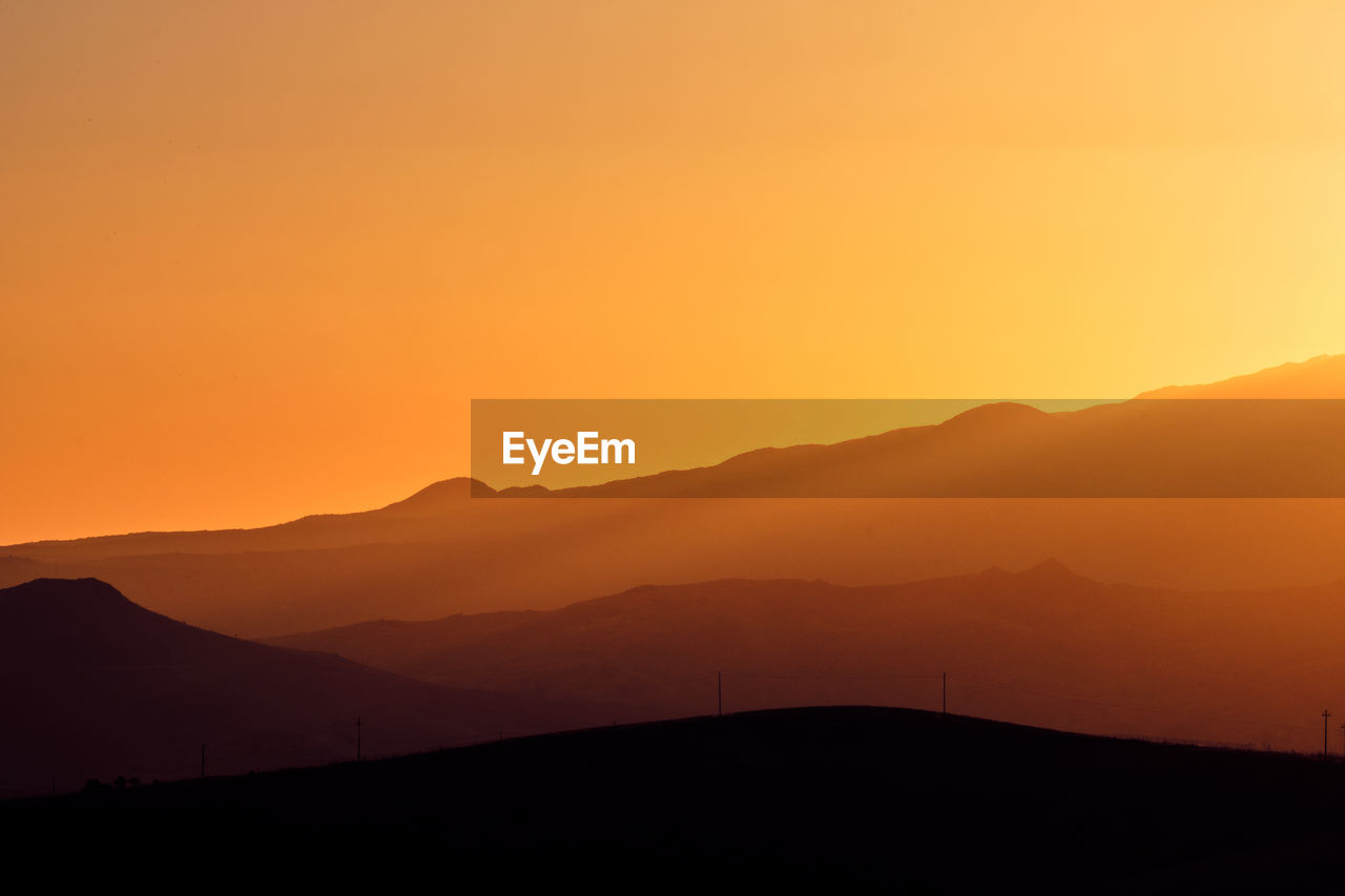 Scenic view of silhouette mountains against orange sky