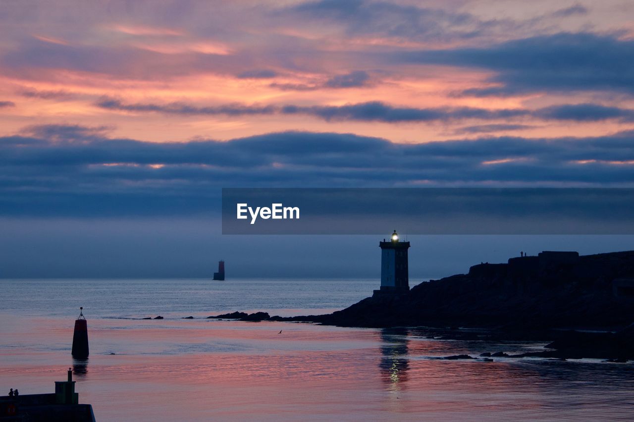 Lighthouse by sea against sky during sunset