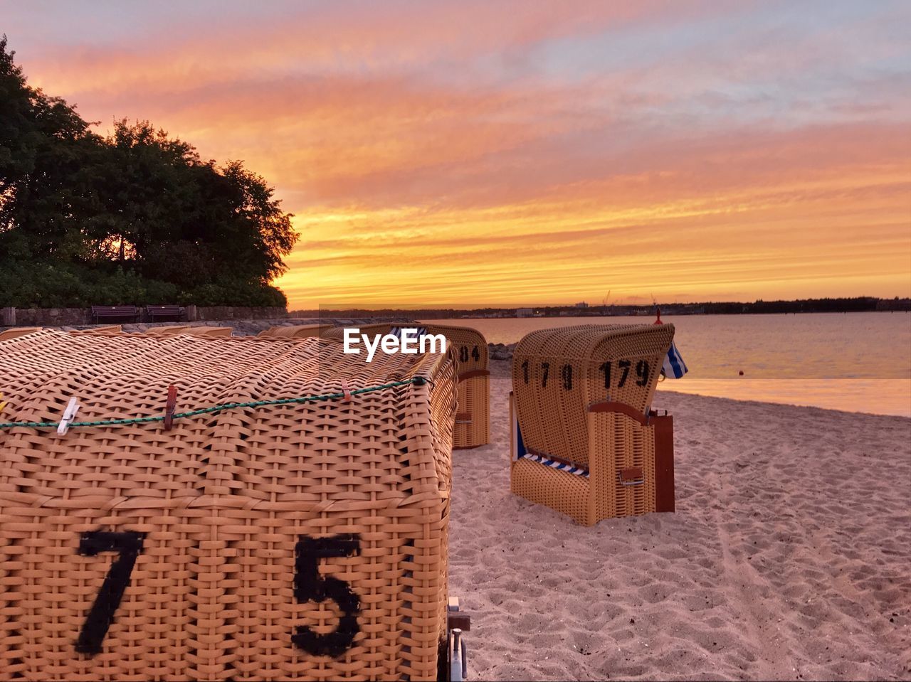 Hooded chairs on beach against sky during sunset