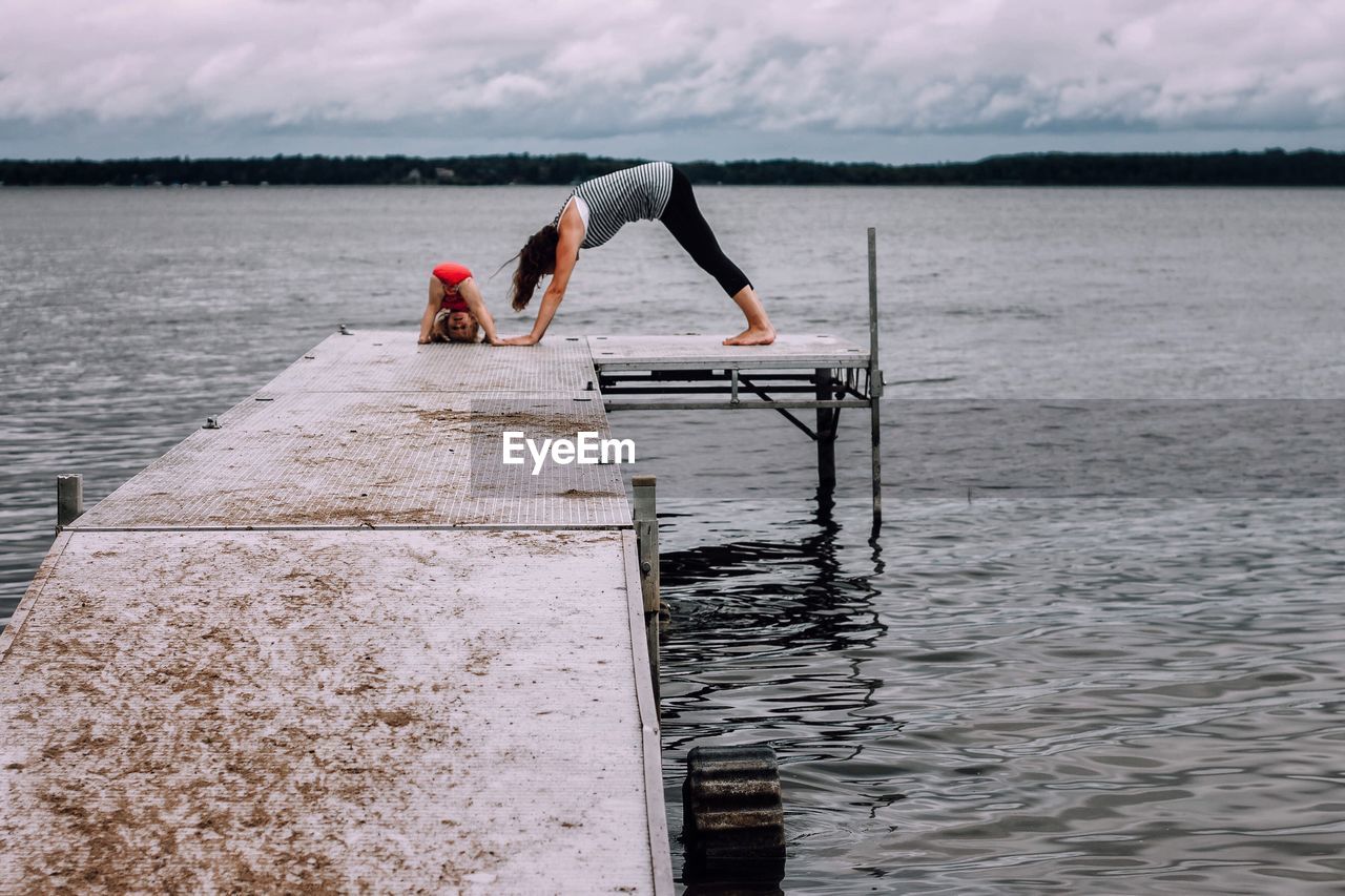 Young woman with daughter doing yoga on pier over lake